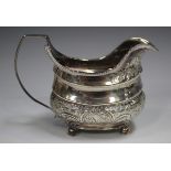 A George III silver cream jug of cushion form with gadrooned rim above a band of foliate scrolls,