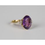 A gold ring, claw set with an oval cut amethyst between diamond set three stone shoulders,