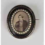A Victorian black enamelled and seed pearl set oval mourning brooch, glazed with a photographic