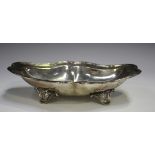 An Edwardian silver dish of lobed oval form with reed and ribbon rim, on four scroll feet, London