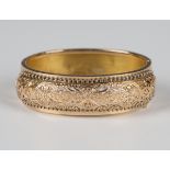 A rose gold oval hinged bangle, circa 1900, the front with pierced and engraved decoration, on a
