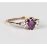 A gold, magenta sapphire and diamond three stone ring, claw set with the oval cut magenta sapphire