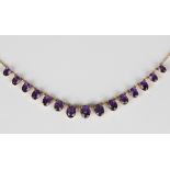 A gold and amethyst necklace, circa 1910, claw set with a row of graduated oval cut amethysts, on