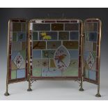 A late Victorian Aesthetic Movement brass framed stained glass triptych firescreen, the three leaded