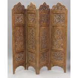 A late 20th century Indian hardwood four-fold dressing screen, profusely carved with panels of birds