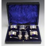 A George V silver seven-piece condiment set of oval form, comprising four salts, each raised on