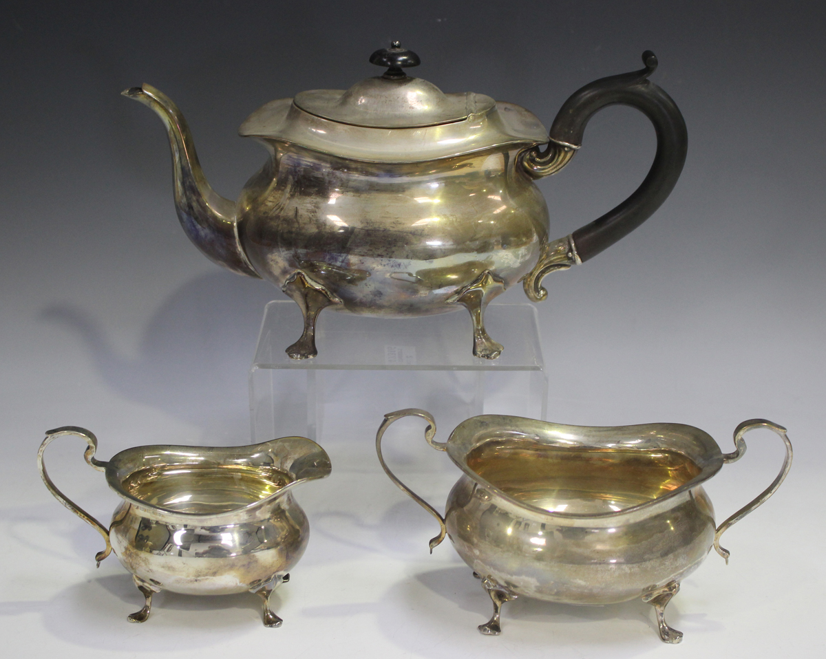 A George V silver three-piece tea set of cushion form, raised on scroll legs, comprising teapot,