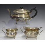 A George V silver three-piece tea set of cushion form, raised on scroll legs, comprising teapot,