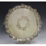 A late Victorian silver circular salver with raised 'C' scroll and scallop shell rim framing an