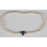 A single row necklace of uniform cultured pearls on a sapphire clasp, designed as a heart, pavé