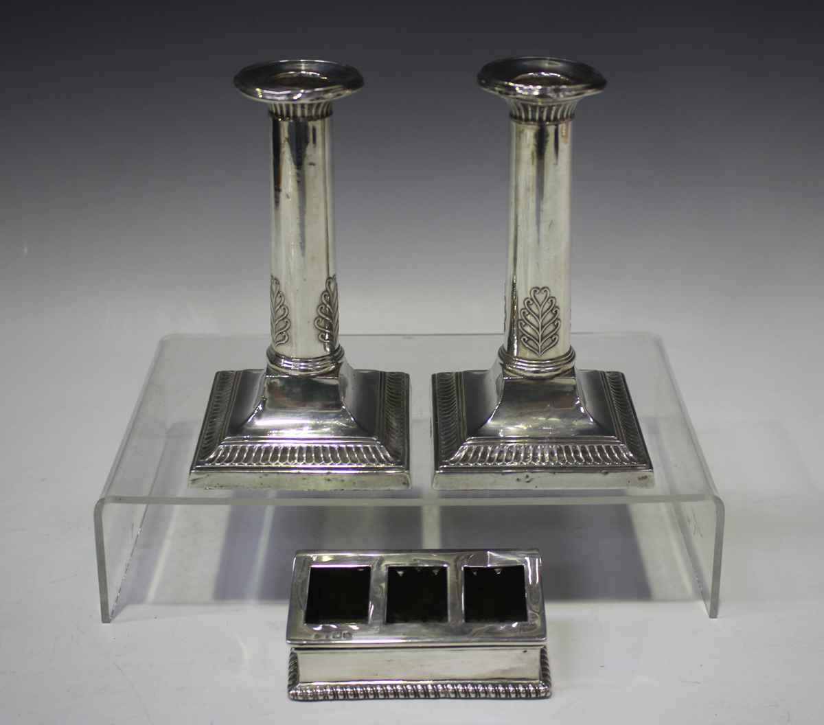 A pair of George V silver candlesticks, each cylindrical stem with anthemion decoration, on a square