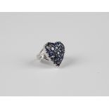 A white gold and sapphire ring in a heart shaped cluster design, mounted with circular cut