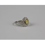 A platinum, yellow sapphire and diamond cluster ring, collet set with the cushion cut yellow