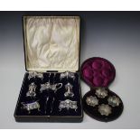 An Edwardian silver seven-piece condiment set of cushion form on scroll legs, comprising four salts,