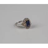 A sapphire and diamond cluster ring, the oval cushion cut sapphire within a surround of twelve