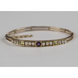 A gold, amethyst, peridot and seed pearl bangle, the front mounted with a circular cut amethyst