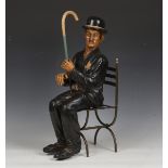 A mid/late 20th century cast painted resin model of Charlie Chaplin, seated on an 'X'-frame chair,