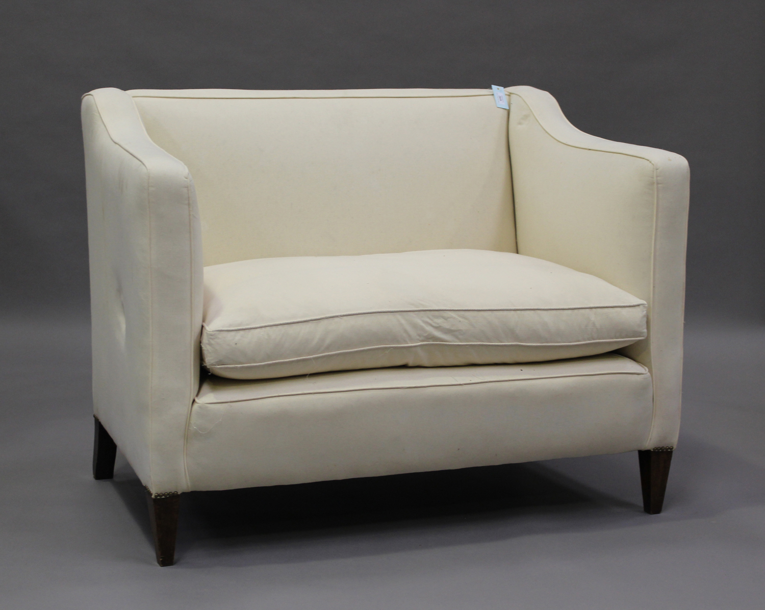 An early 20th century two-seat wing back settee, upholstered in calico, on square tapering block