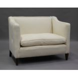 An early 20th century two-seat wing back settee, upholstered in calico, on square tapering block