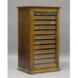 An early 20th century oak collector's cabinet, the glazed door enclosing twelve sliding trays,