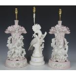 A pair of bisque porcelain table lamps, modelled as a lady and gallant seated beside trees, height