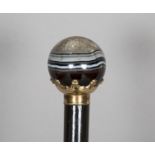 A late 19th century ebonized walking cane, the spherical banded agate handle with gilt metal collar,