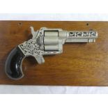 A crescent toy clover leaf model of a four shot revolver mounted on a wooden plaque