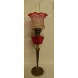 An Edwardian tall brass and copper oil lamp with cranberry-tinted glass reservoir and