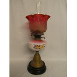 A Victorian brass oil lamp with opaque glass floral reservoir and cranberry-tinted floral shade on