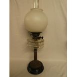 A Victorian brass column oil lamp with clear glass reservoir and pink-tinted glass shade on ceramic