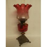 A Victorian cast iron and brass oil lamp with cranberry-tinted glass reservoir and cranberry-tinted