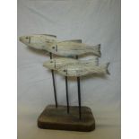 A modern display of four painted wooden swimming fish on metal stems and rustic base,