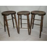 Three various old elm and beech laboratory-style stools with shaped oval seats on turned legs (af)
