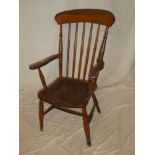 An old elm and beech spindle back kitchen carver armchair with shaped seat on turned tapered legs