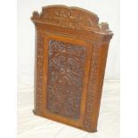 A late Victorian carved oak hanging corner cupboard with shelves enclosed by a decorated panel door,
