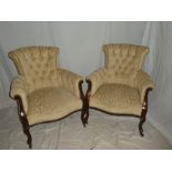 A pair of late Victorian carved mahogany easy chairs upholstered in cream buttoned fabric on