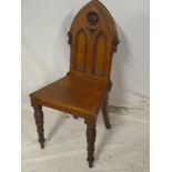 A Victorian carved oak Gothic-style hall chair with panelled back on turned tapered legs