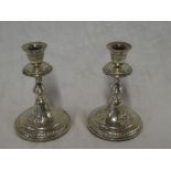 A pair of Continental silvered tapered candlesticks with raised floral decoration on circular bases,