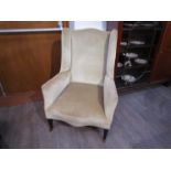 An Edwardian wingback fireside armchair on square tapering legs and ceramic castors