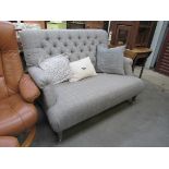 A tweed design grey upholstered two seater sofa with button back, turned legs to castors,