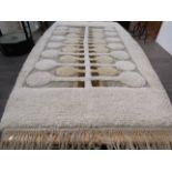 A karakul wool rug with relief woven roundels in cream, tan brown and blue, tasseled ends.