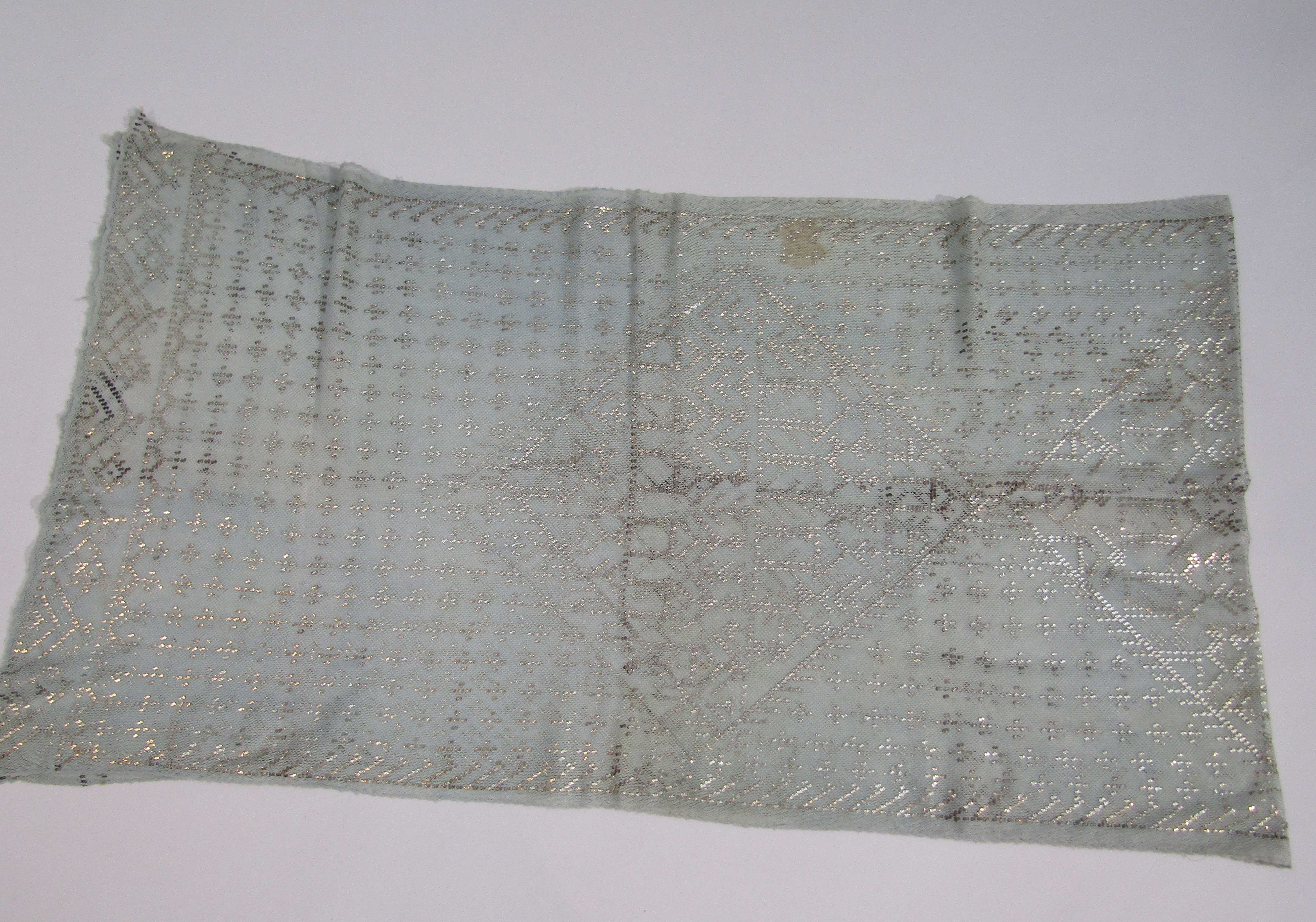 An Assuit shawl made using pale blue cotton net decorated with silver metal design; 210cm x 60cm.