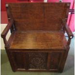 An early 20th Century oak monks bench with carved rosettes to top and carved floral middle panel,
