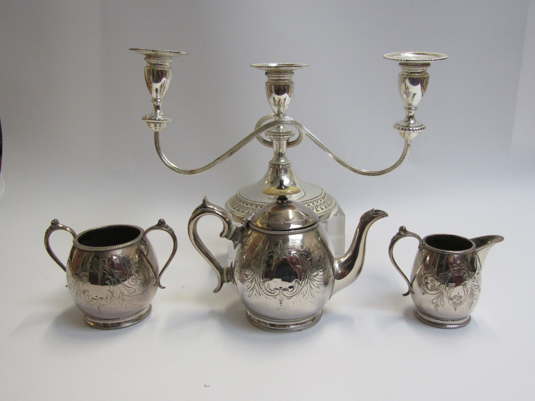 A silver plate three piece tea set and candlestick