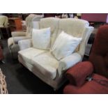 A modern wingback two seater sofa with loose cushions in cream velour upholstery