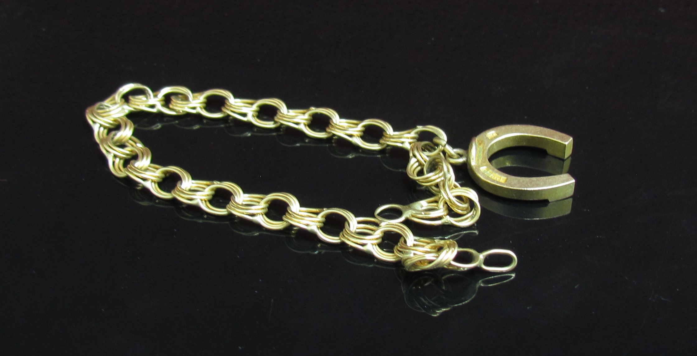 A 9ct gold horseshoe hung on a loop bracelet, 17cm long, 8.