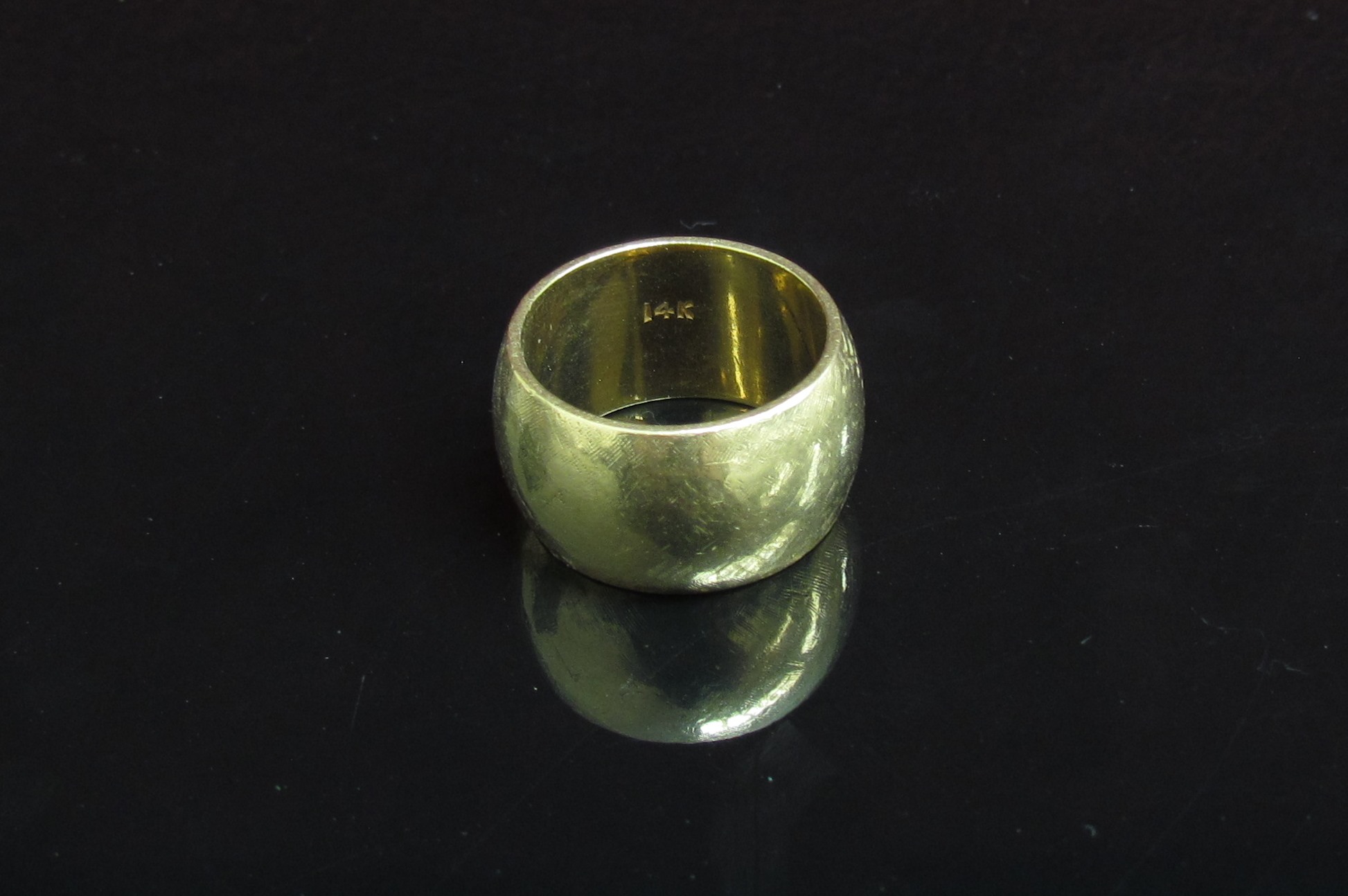 A gold band 11mm wide stamped 14k. Size O, 15.