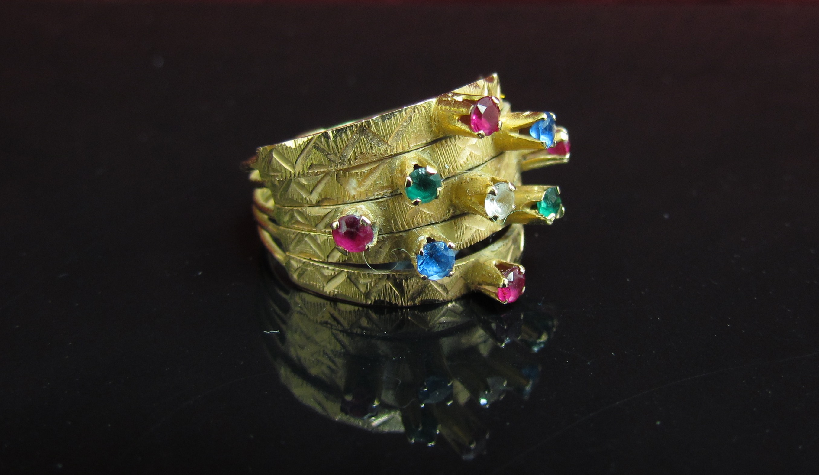 A gold ring with five bands all set with coloured stones. Size O, 4.