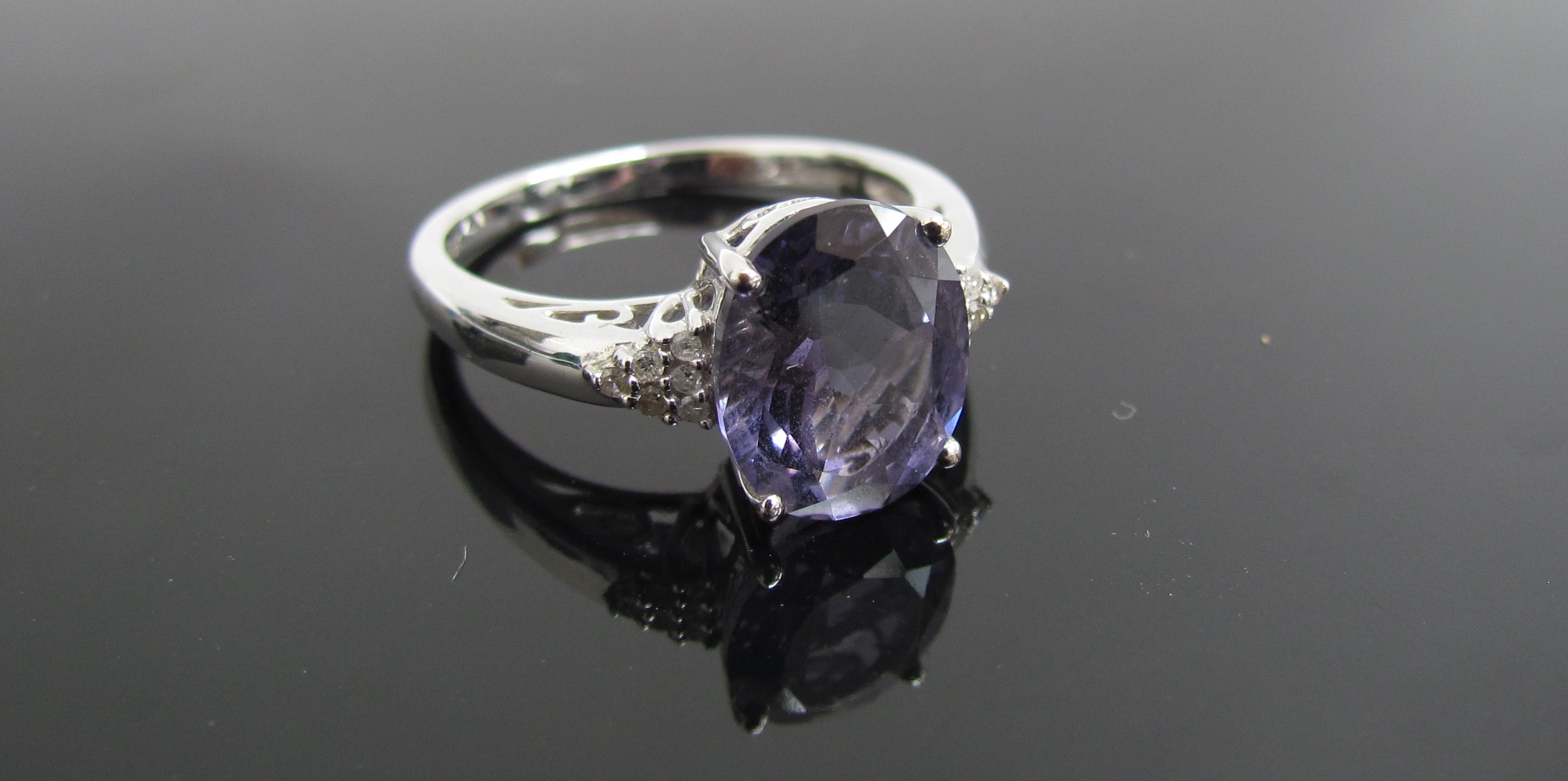 A 9ct white gold ring with oval purple stone flanked by diamond set shoulders. Size R, 3.