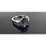 A 9ct white gold ring with oval purple stone flanked by diamond set shoulders. Size R, 3.